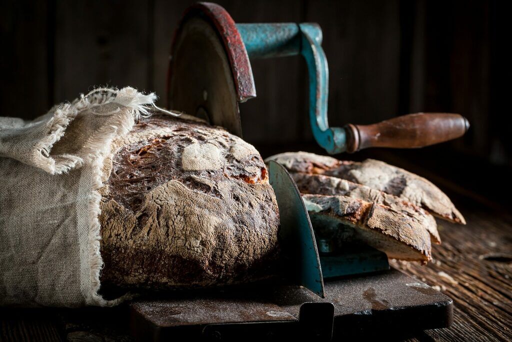 Tasty loaf of bread on slicer with on dark table