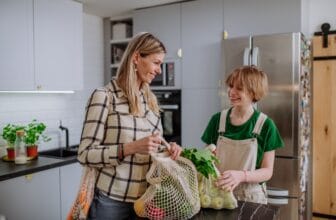 Mother unpacking local food in zero waste packaging from bag with help of daughter in kitchen at