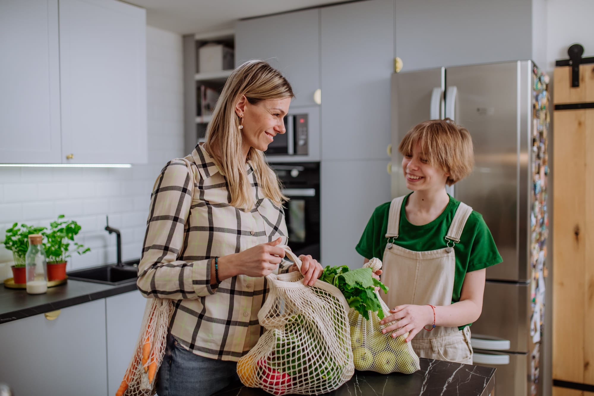 Zero-Waste-Kochen – Nachhaltig & clever: So reduzierst du Küchenabfälle auf ein Minimum 1 - Küchenhelferlein Mother unpacking local food in zero waste packaging from bag with help of daughter in kitchen at
